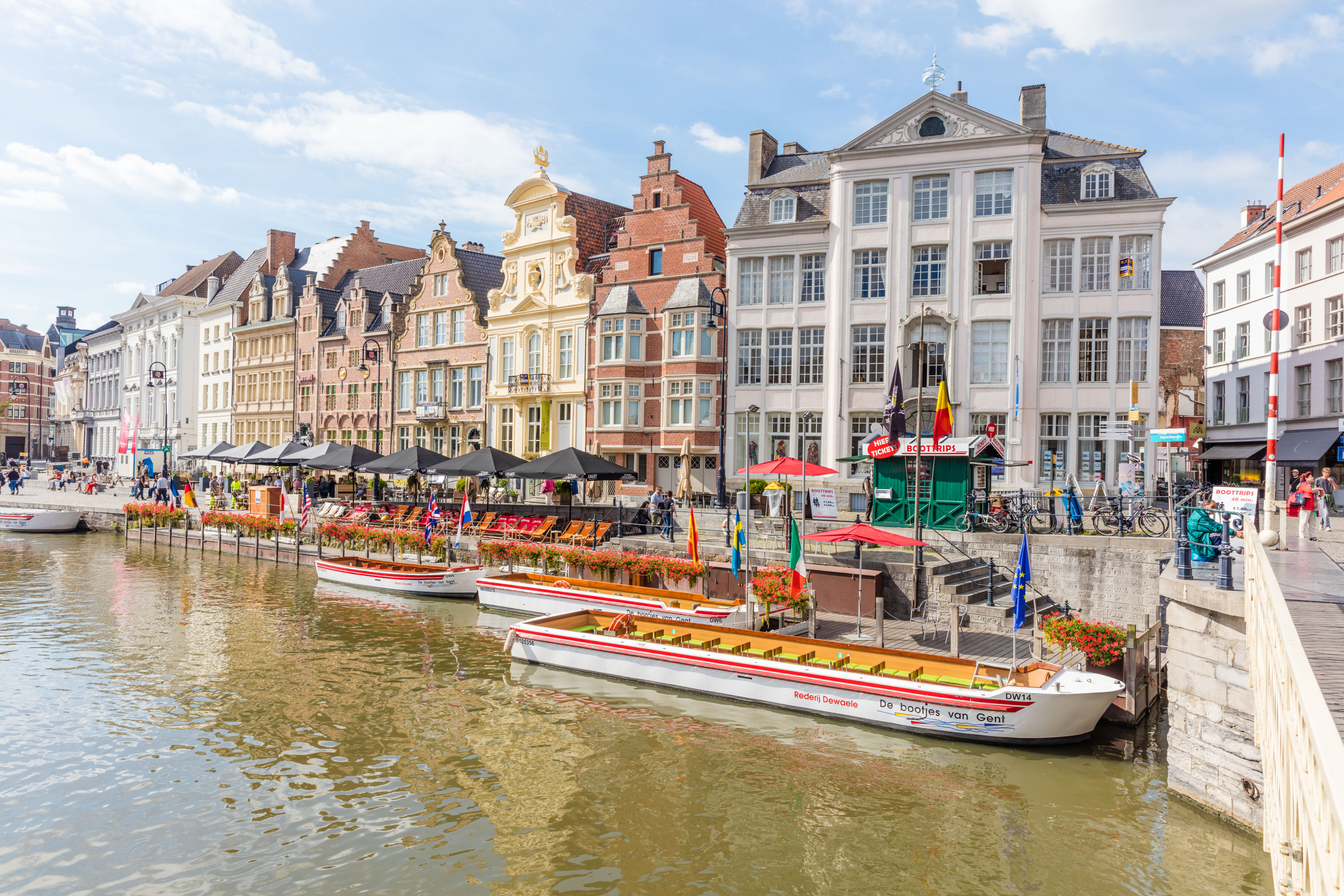 Tour boats and cafes along a canal Canal with tour boats docked beside outdoor cafes and historic buildings on a sunny day.