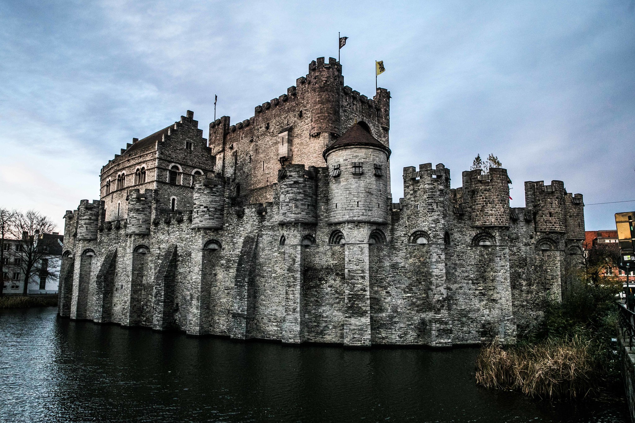 Medieval stone castle by a moat Medieval stone castle with round towers and battlements beside a moat under a cloudy sky.