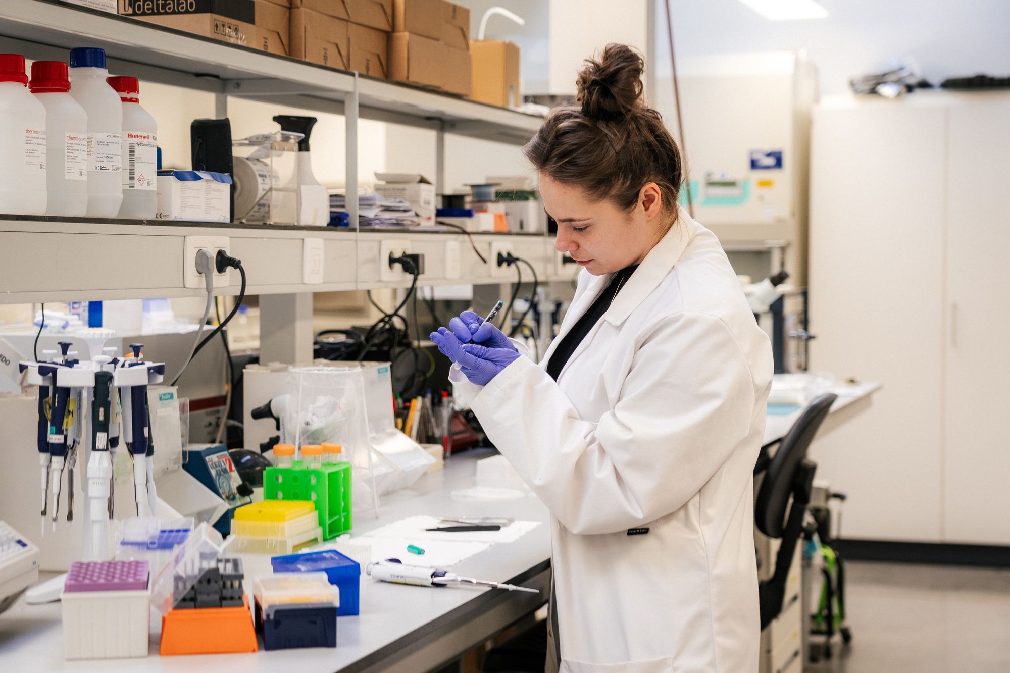 Scientist labeling a sample in the lab Scientist in a lab coat and gloves labeling a sample at a laboratory bench with pipettes and tubes.