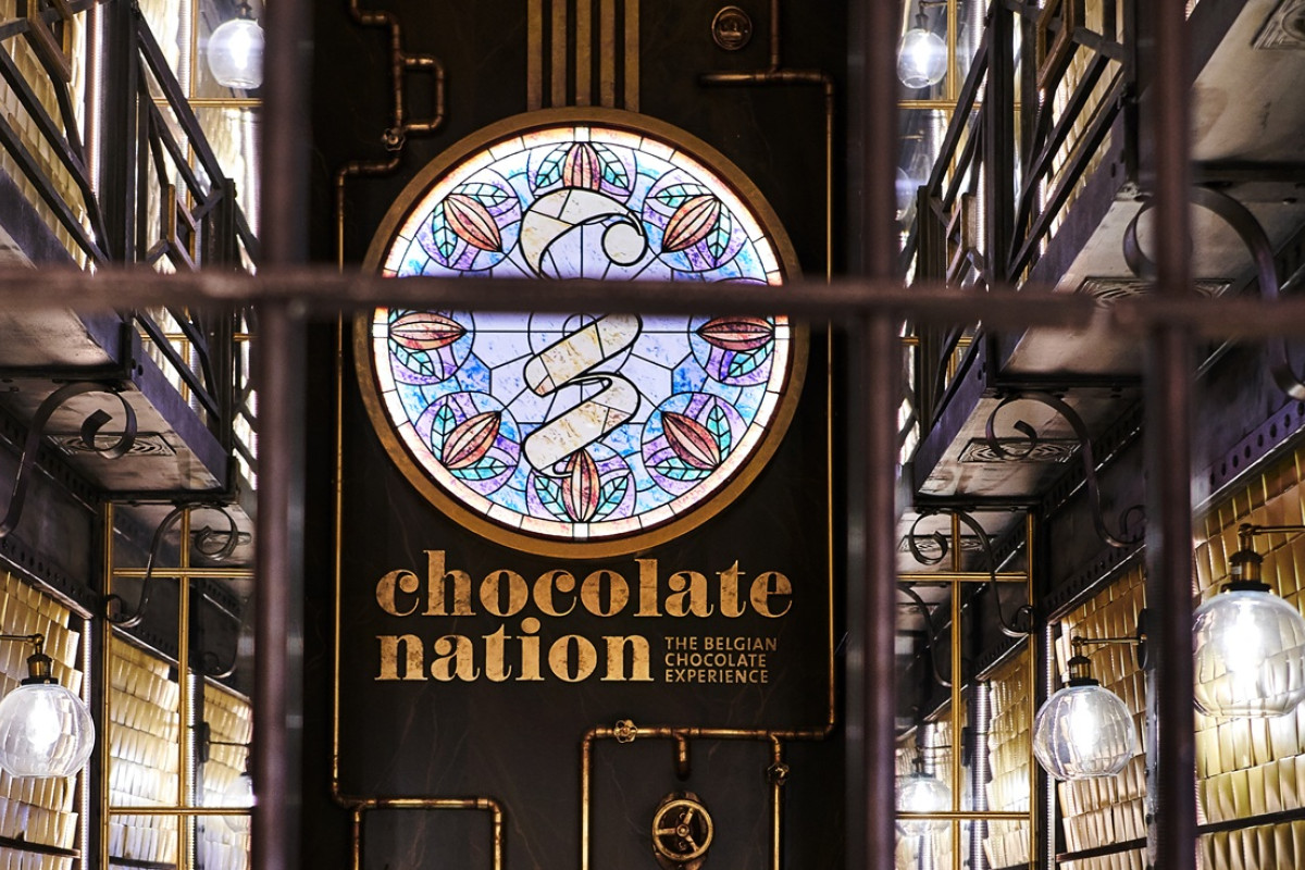 Chocolate Nation museum interior sign Interior view of Chocolate Nation museum entrance with stained glass sign, industrial pipes, and hanging lights.